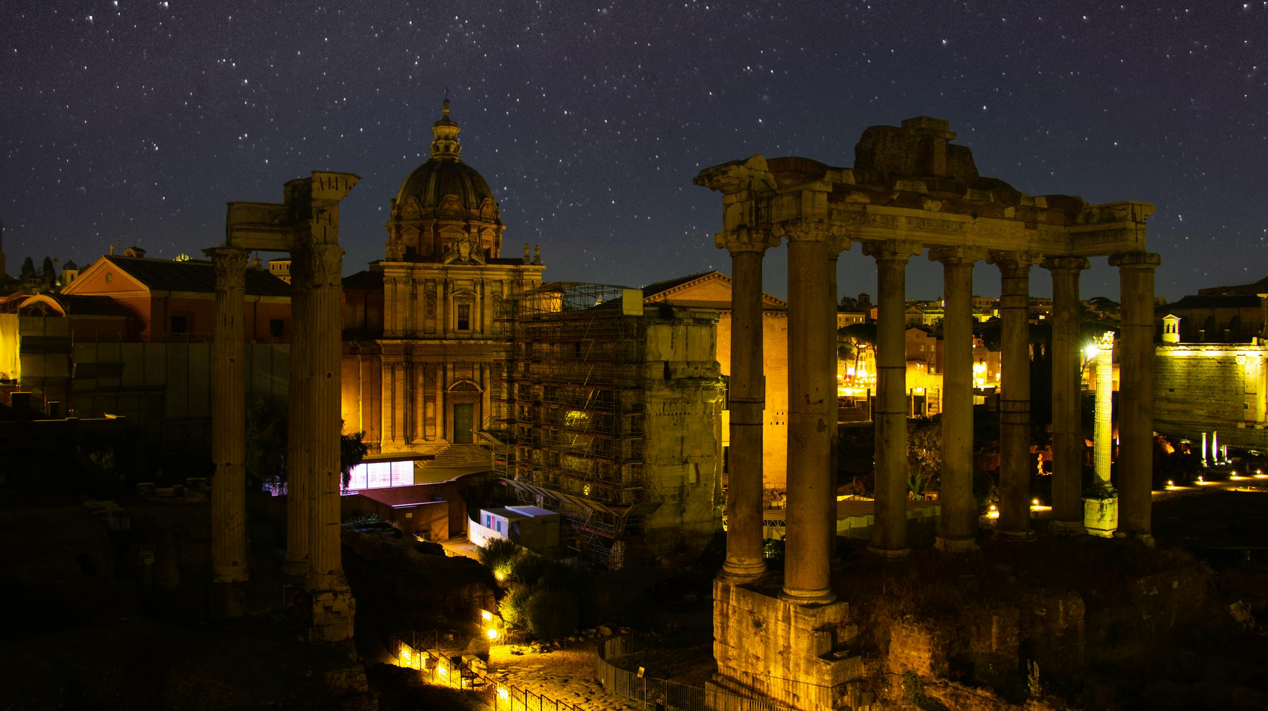 Breathtaking night scene of the illuminated Roman Forum in Rome, showcasing ancient architecture under a starry sky.